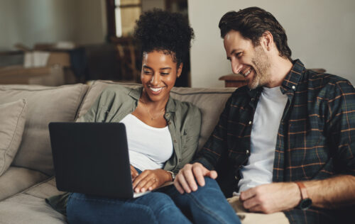 a man and woman sitting on a couch looking at a laptop