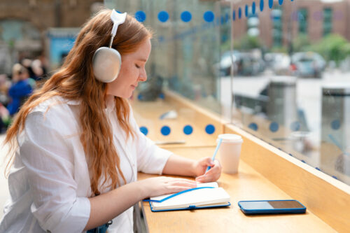 a woman wearing headphones and writing on a notebook
