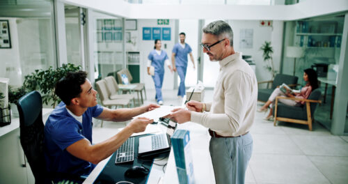 Hospital, nurse and man at front desk with paperwork for appointment, consultation and medical service. Healthcare, clinic and mature patient with admin for insurance, application form and documents.